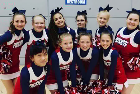 Eine Gruppe von Cheerleadern in einheitlichen Uniformen posiert vor einem Toilettenschild auf dem Gelände der American Heritage Academy.