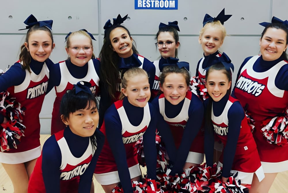 Eine Gruppe von Cheerleadern in einheitlichen Uniformen posiert vor einem Toilettenschild auf dem Gelände der American Heritage Academy.