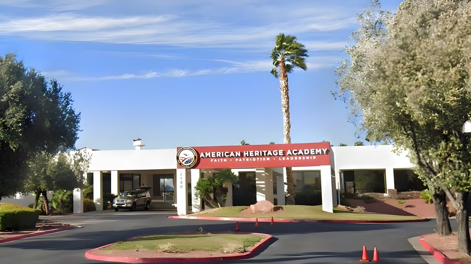Das Gebäude der American Heritage Academy mit rotem Schild und Palmen im Vordergrund unter klarem blauem Himmel.