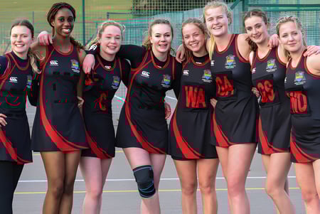 Ein Team von Athletinnen in schwarzen und roten Uniformen posiert gemeinsam auf dem Sportplatz des Ampleforth College.