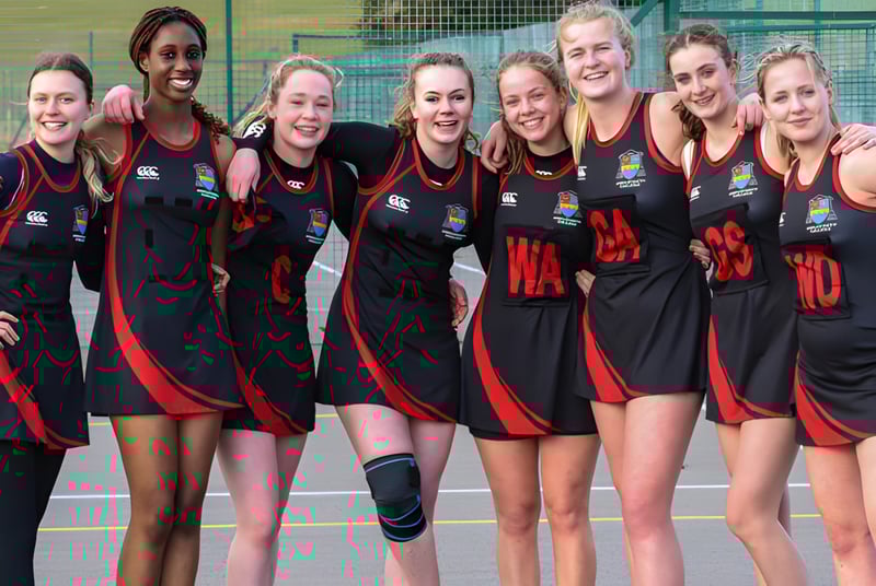Ein Team von Athletinnen in schwarzen und roten Uniformen posiert gemeinsam auf dem Sportplatz des Ampleforth College.