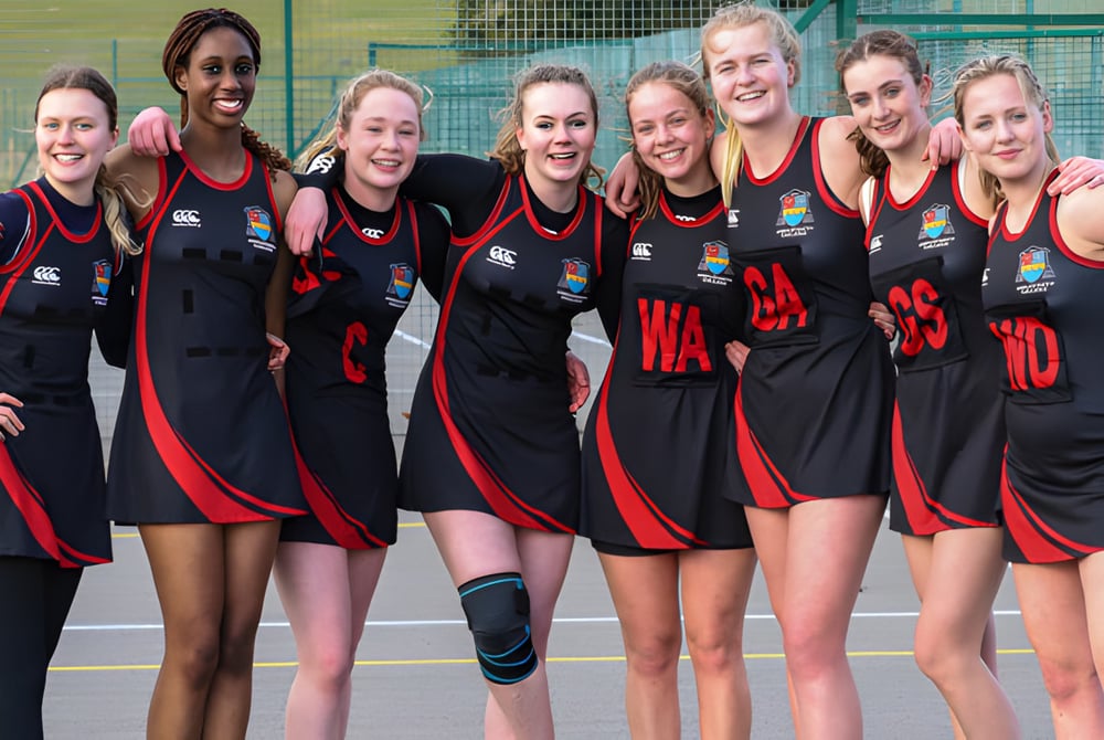 Ein Team von Athletinnen in schwarzen und roten Uniformen posiert gemeinsam auf dem Sportplatz des Ampleforth College.