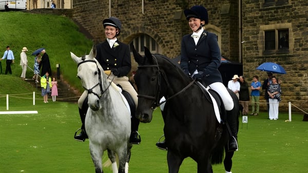 Zwei Reiter in formeller Kleidung stehen mit Pferden auf einer Wiese vor einem Backsteingebäude des Ampleforth College.