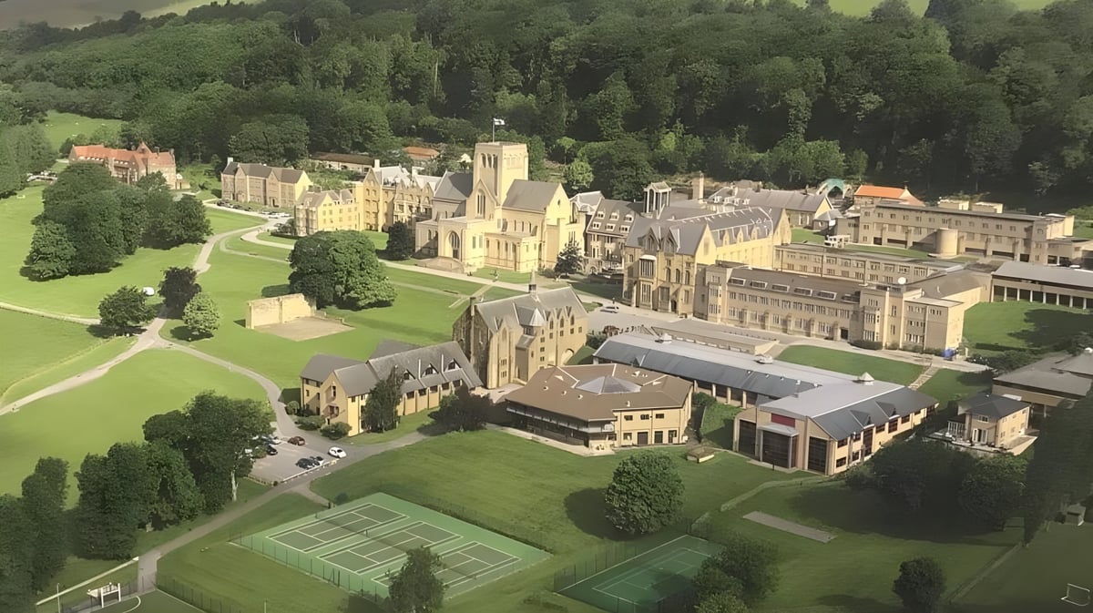 Das Ampleforth College zeigt ein weites mittelalterliches Schloss mit gepflegten Rasenflächen und Tennisplätzen im Vordergrund.