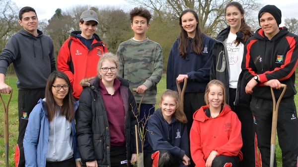 Eine Gruppe Schülerinnen und Schüler des Ampleforth College steht zusammen im Außenbereich vor Bäumen und Grünflächen.