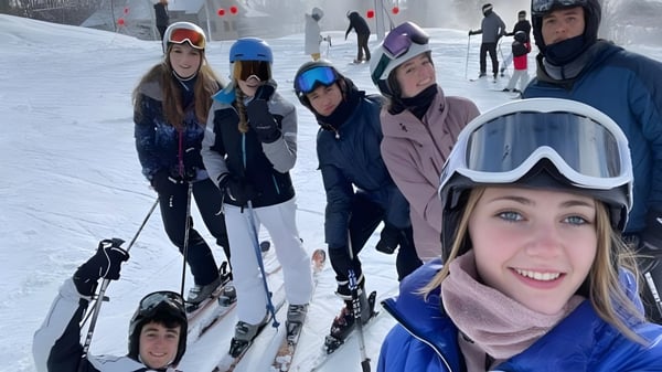 Schüler der Andrews Osborne Academy stehen mit Skiausrüstung auf einer verschneiten Piste mit Skiliften im Hintergrund.