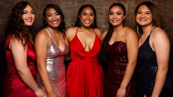 Fünf Schülerinnen des Aorere College posieren in glamourösen Abendkleidern vor einem warmen, strukturierten Hintergrund.