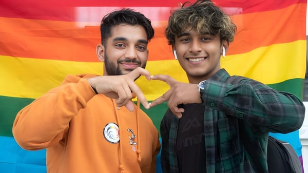 Zwei Schüler des Aorere College posieren vor einem bunten Regenbogen-Hintergrund und lächeln.