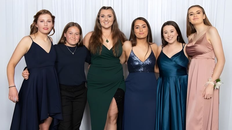 Eine Gruppe von sechs Schülerinnen in unterschiedlichen Abendroben auf dem Campus des Aotea College vor weißem Hintergrund.