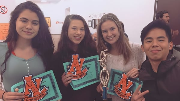 Eine Gruppe von vier Schülern der Apple Valley Christian School hält bunte Plakate in einem Innenraum hoch.