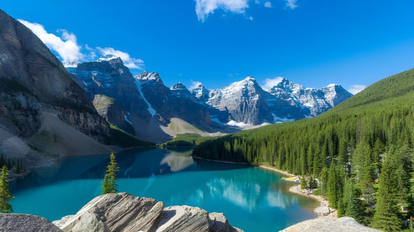 Ein ruhiger türkisfarbener Bergsee vor schneebedeckten Gipfeln und immergrünen Wäldern auf dem Gelände von Appleby College.