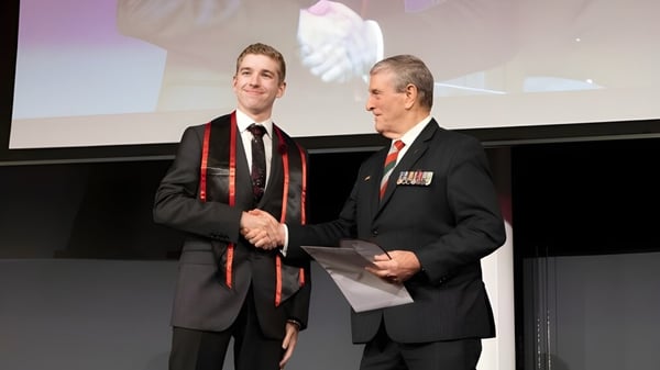 Zwei Männer in formeller Kleidung geben sich auf der Bühne die Hand vor einer Projektionsleinwand auf dem Campus der Applecross Senior High School.