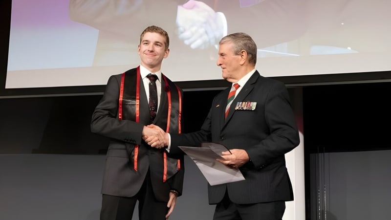 Zwei Männer in formeller Kleidung geben sich auf der Bühne die Hand vor einer Projektionsleinwand auf dem Campus der Applecross Senior High School.
