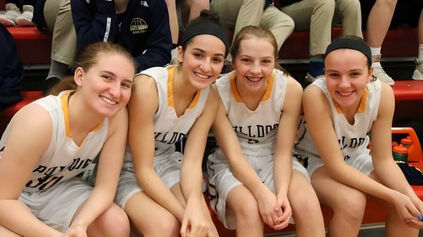 Vier Schülerinnen der Aquin High School sitzen als Basketballteam zusammen und lächeln.