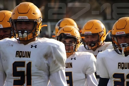 Eine Gruppe von Fußballspielern der Aquin High School trägt weiße Trikots und steht gemeinsam auf dem Spielfeld.