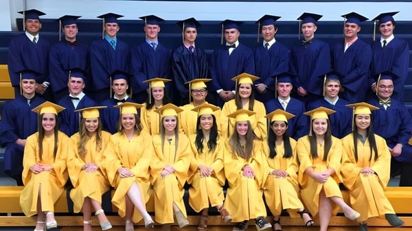 Absolventinnen und Absolventen der Aquin High School in blauen und gelben Talaren vor einem gelben Hintergrund.