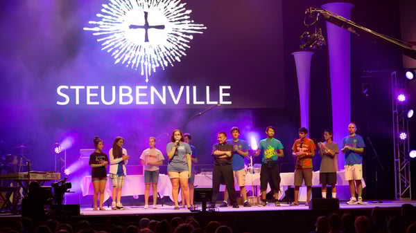 Schüler der Aquin High School stehen auf der Bühne vor einer großen Kreuz-Lichtinstallation mit dem Schriftzug STEUBENVILLE.