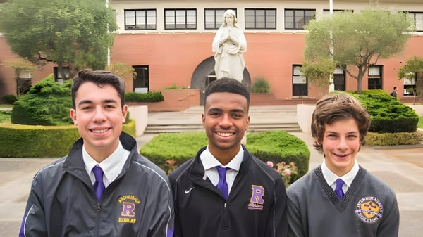 Drei Schüler in Schuluniformen stehen vor einer Statue auf dem Campus der Archbishop Riordan High School.