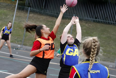 Zwei Schülerinnen der Archbishop's School spielen ein Netballspiel auf dem Spielfeld der Schule.