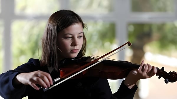 Eine Schülerin der Archbishop's School spielt konzentriert Violine vor unscharfem Naturhintergrund.