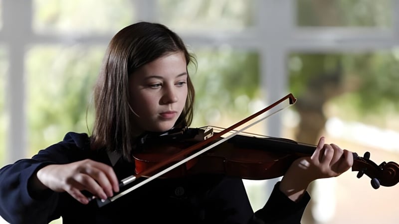 Eine Schülerin der Archbishop's School spielt konzentriert Violine vor unscharfem Naturhintergrund.