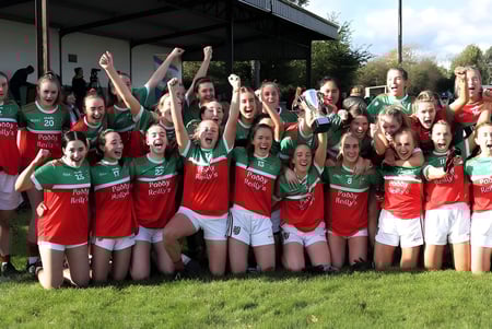 Eine Gruppe junger Athletinnen der Ardscoil Phadraig feiert gemeinsam auf einem Grasfeld.