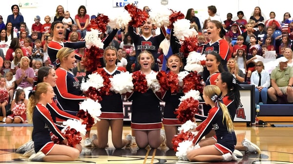Eine Gruppe von Cheerleadern der Arendell Parrott Academy führt eine Darbietung auf dem Basketballfeld vor zahlreichen Zuschauern auf.