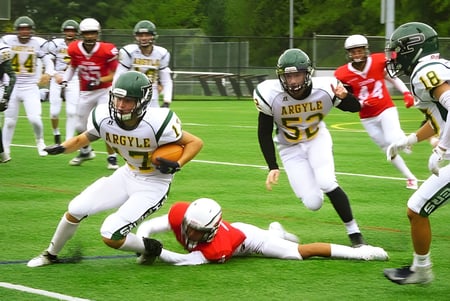 Schüler der Argyle Secondary School spielen ein Footballspiel und führen während des Spiels einen Tackle auf dem Spielfeld aus.