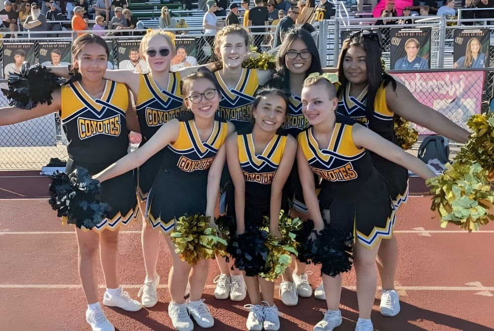Eine Gruppe Cheerleader in gelben und schwarzen Uniformen posiert auf dem Sportfeld der Arizona Lutheran Academy.