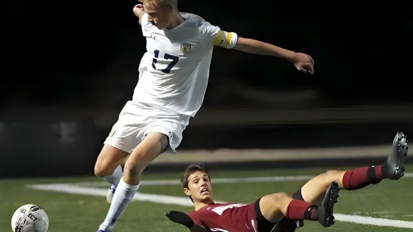 Ein Fußballspieler in weißem Trikot springt über einen Spieler in rotem Trikot auf dem Spielfeld der Arlington High School.