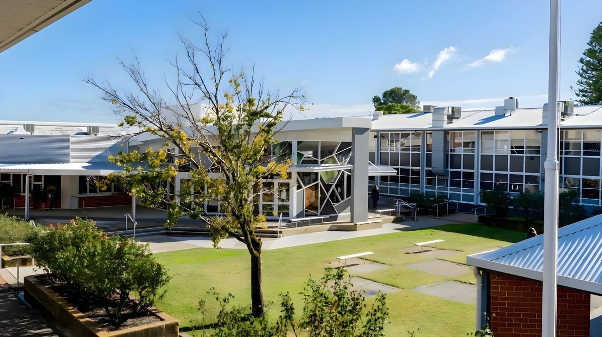 Der Innenhof der Armadale Senior High School zeigt einen blühenden Baum und moderne Gebäude mit großen Fenstern bei klarem Himmel.