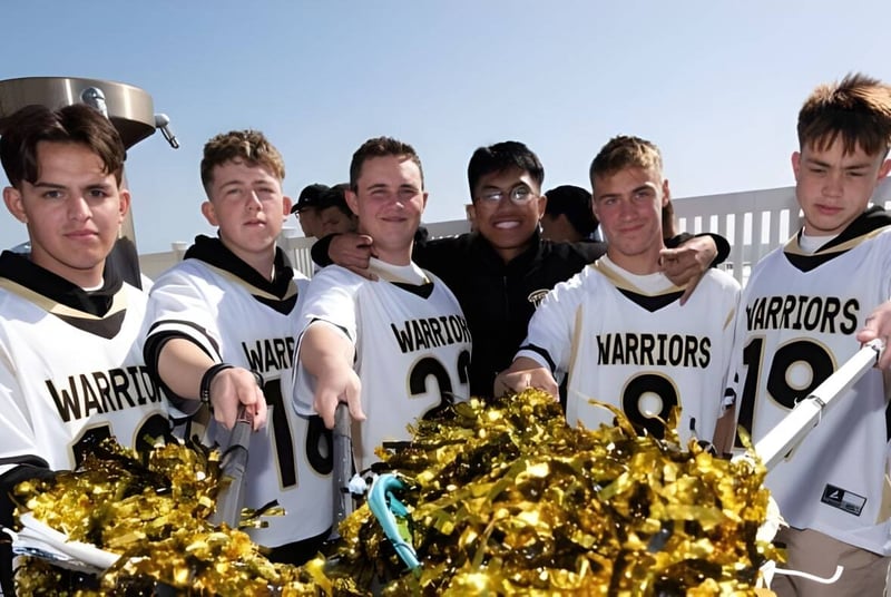 Eine Gruppe junger Athleten der Army and Navy Academy steht im Freien in weißen und schwarzen Sportuniformen mit dem Schriftzug Warriors und hält goldene Pompons.