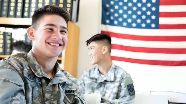 Zwei lächelnde Militärangehörige in Uniform stehen vor der amerikanischen Flagge auf dem Gelände der Army and Navy Academy.