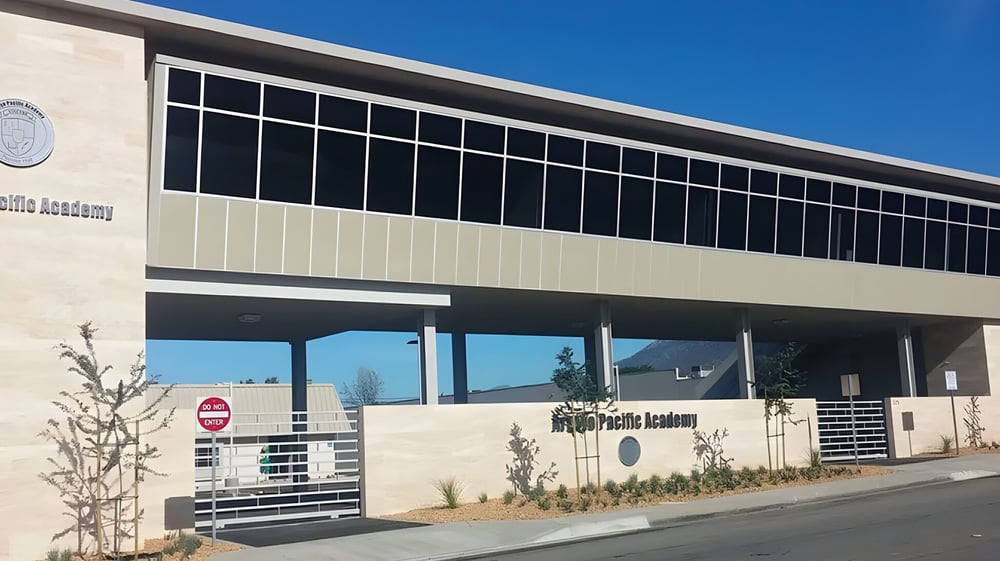 Das mehrstöckige moderne Hauptgebäude der Arroyo Pacific Academy mit großen Fenstern vor klarem blauen Himmel.