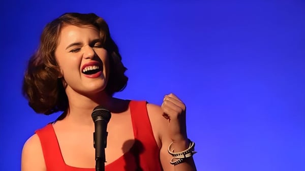 Eine Schülerin der Arroyo Pacific Academy singt leidenschaftlich in ein Mikrofon vor blauem Hintergrund.