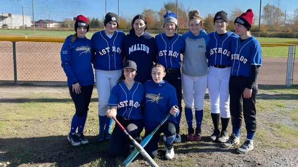 Eine Gruppe junger Athletinnen steht in blauen Uniformen gemeinsam auf dem Baseballfeld der Ascension Collegiate.