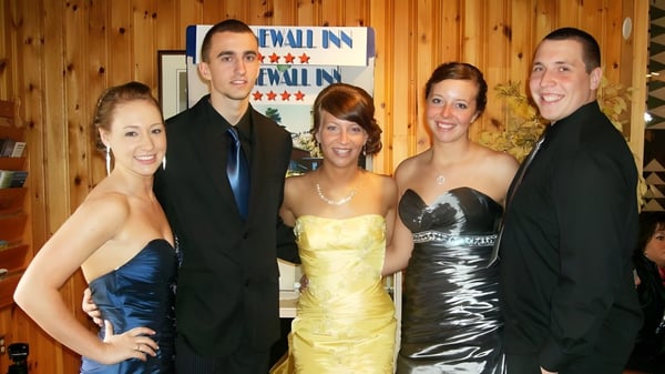 Eine Gruppe von fünf Personen posiert vor der Holzwand mit Wall Inn Schild auf dem Gelände des Ascension Collegiate.