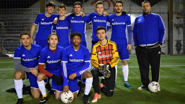 Die Fußballmannschaft des Ashbourne College posiert in blauen Trikots für ein Mannschaftsfoto auf dem Sportplatz bei Nacht.