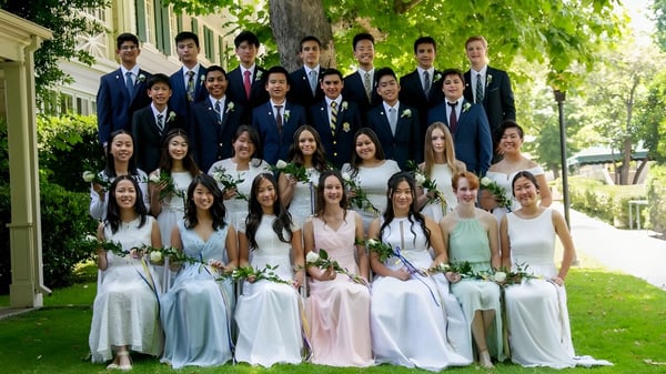 Eine Gruppe von Schülerinnen und Schülern des Ashbury College steht in formeller Kleidung in einer grünen Außenanlage mit Bäumen im Hintergrund.