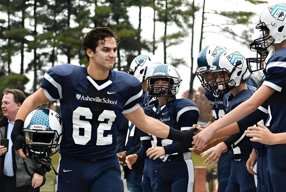 Eine Gruppe von Fußballspielern der Asheville School grüßt sich auf einem Spielfeld mit Baumbestand.