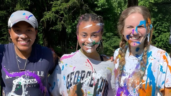 Drei Schülerinnen und Schüler mit bunter Farbe auf Gesicht und Kleidung stehen auf dem Gelände der Asheville School.