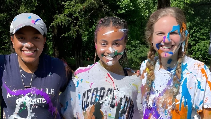 Drei Schülerinnen und Schüler mit bunter Farbe auf Gesicht und Kleidung stehen auf dem Gelände der Asheville School.