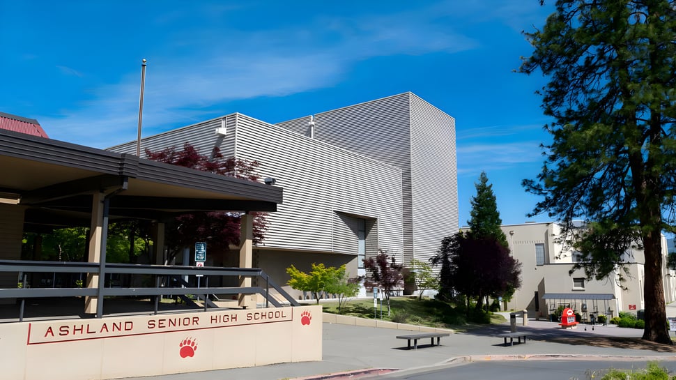 Das moderne Schulgebäude mit überdachtem Gehweg im Ashland School District ist von Bäumen und klarem Himmel umgeben.