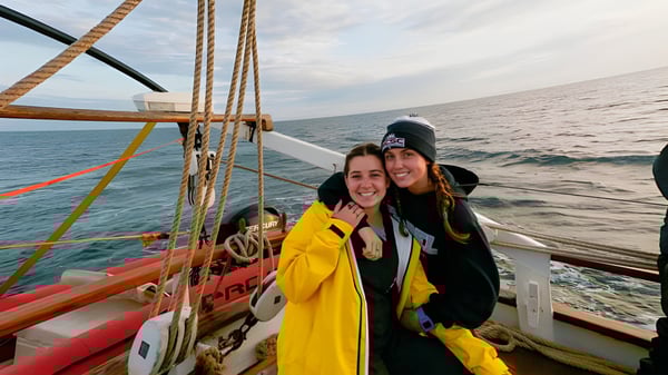 Zwei Schülerinnen der Ashley Hall School stehen auf dem Deck eines Segelbootes mit offenem Meer und bewölktem Himmel im Hintergrund.