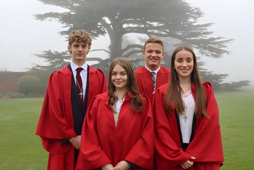 Eine Gruppe von vier Absolventen in roten Talaren steht auf einer Wiese auf dem Campus des Ashville College.
