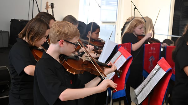 Eine Gruppe junger Musiker der Aspley State High School spielt konzentriert Streichinstrumente während eines Auftritts.