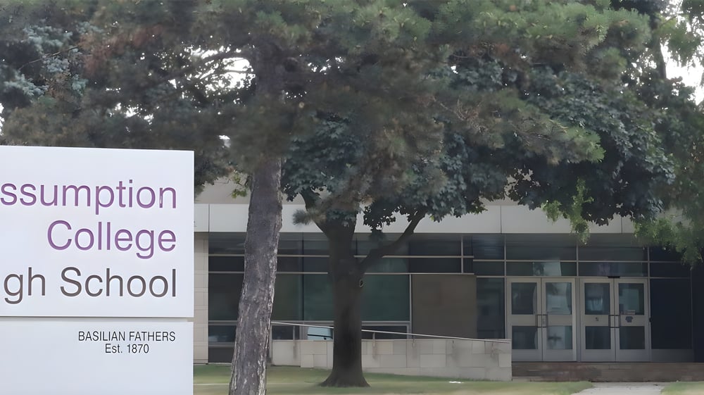 Die Außenansicht von Assumption College Catholic High School mit einem Schild und Baumreihe im Hintergrund.