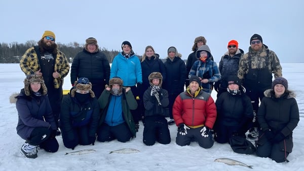Schüler der Assumption College Catholic High School stehen winterlich gekleidet auf einem verschneiten Feld vor einem Wald.
