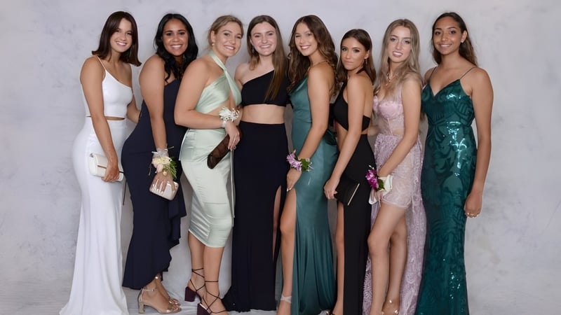 Eine Gruppe Schülerinnen der Assumption Grammar School posiert in Abendkleidern vor weißem Hintergrund.