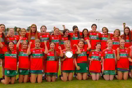 Eine Gruppe junger Fußballspielerinnen steht auf dem Sportplatz der Assumption Grammar School unter einem bewölkten Himmel.